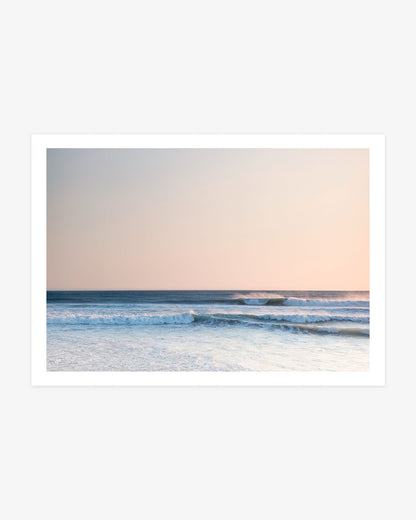 Pacific Ocean sunset wall art featuring layered blue waves beneath a soft peach sky with warm evening light across the water.