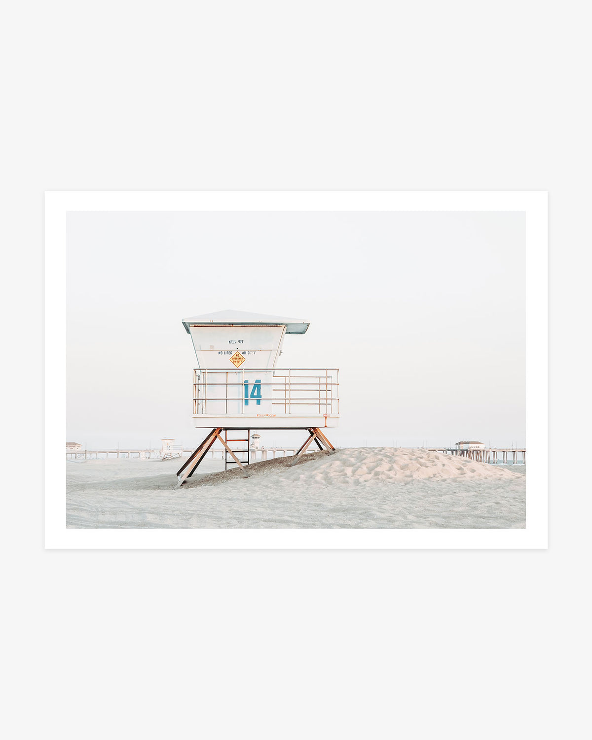 Huntington Beach lifeguard tower wall art featuring Tower 14 on a sandy rise with the pier visible in the distance beneath a pale coastal sky.