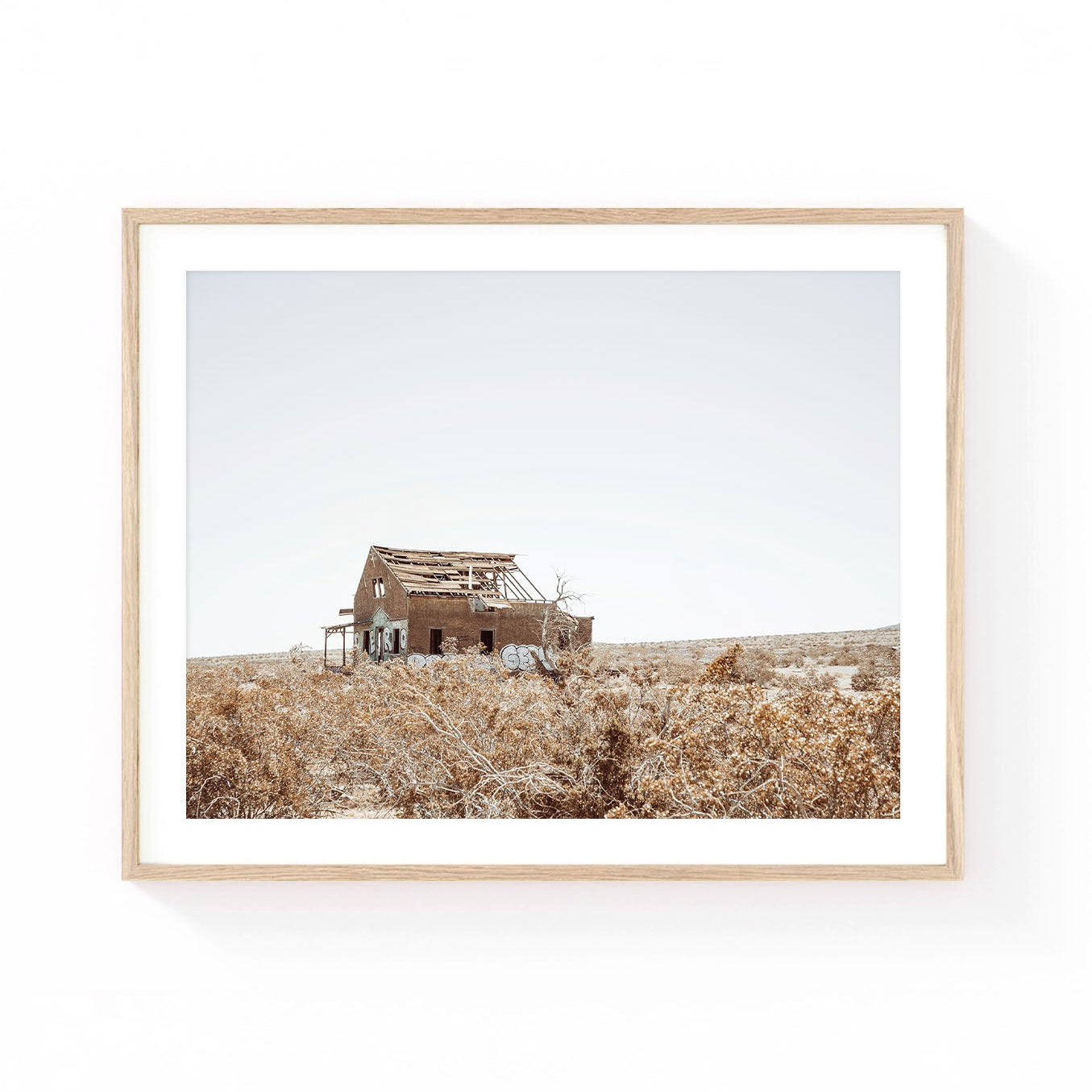 Desert homestead wall art featuring an abandoned rustic house surrounded by dry desert brush and open landscape under a soft neutral sky.