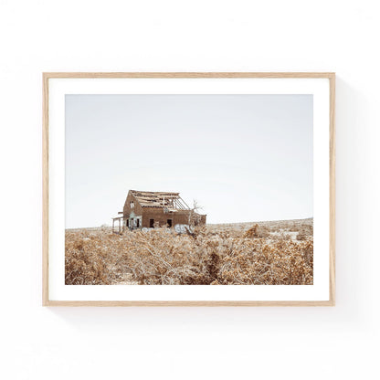 Desert homestead wall art featuring an abandoned rustic house surrounded by dry desert brush and open landscape under a soft neutral sky.