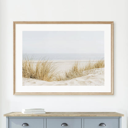 Minimalist coastal wall art print of sandy beach grass in a natural wood frame