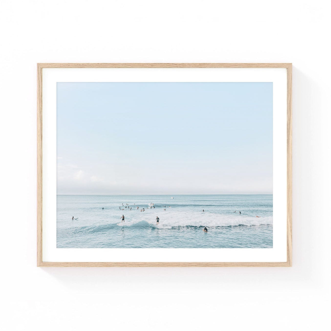 Surf wall art featuring surfers waiting beyond gentle ocean waves beneath a soft blue horizon in calming coastal tones.