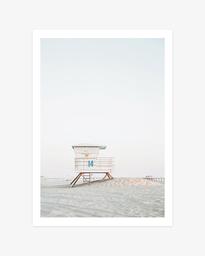 Huntington Beach lifeguard tower wall art featuring Tower 14 on a sandy rise beneath a pale coastal sky, with the pier in the distance.