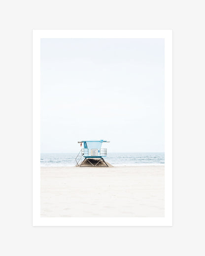 Huntington Beach lifeguard tower wall art featuring blue Tower 8 on a quiet sandy beach against the soft ocean horizon.