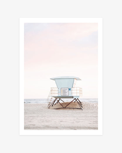 Huntington Beach wall art featuring a pastel blue lifeguard tower on a quiet sandy beach beneath a soft pink California sky.