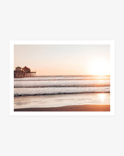 Huntington Beach Pier wall art featuring the former Ruby’s Diner, golden sunset light, ocean waves and reflections across the wet sand.
