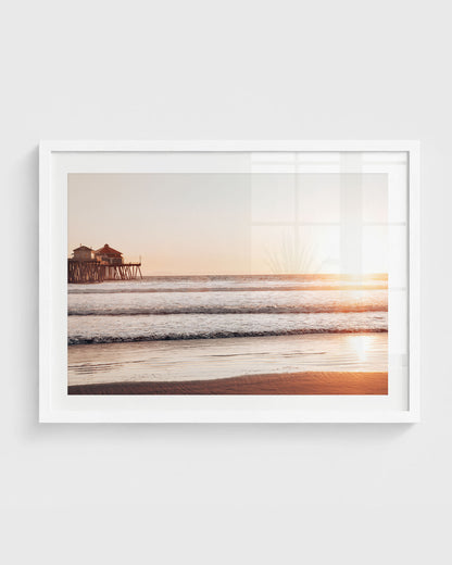Huntington Beach pier at sunset with soft golden light reflecting on ocean waves and sandy shore.