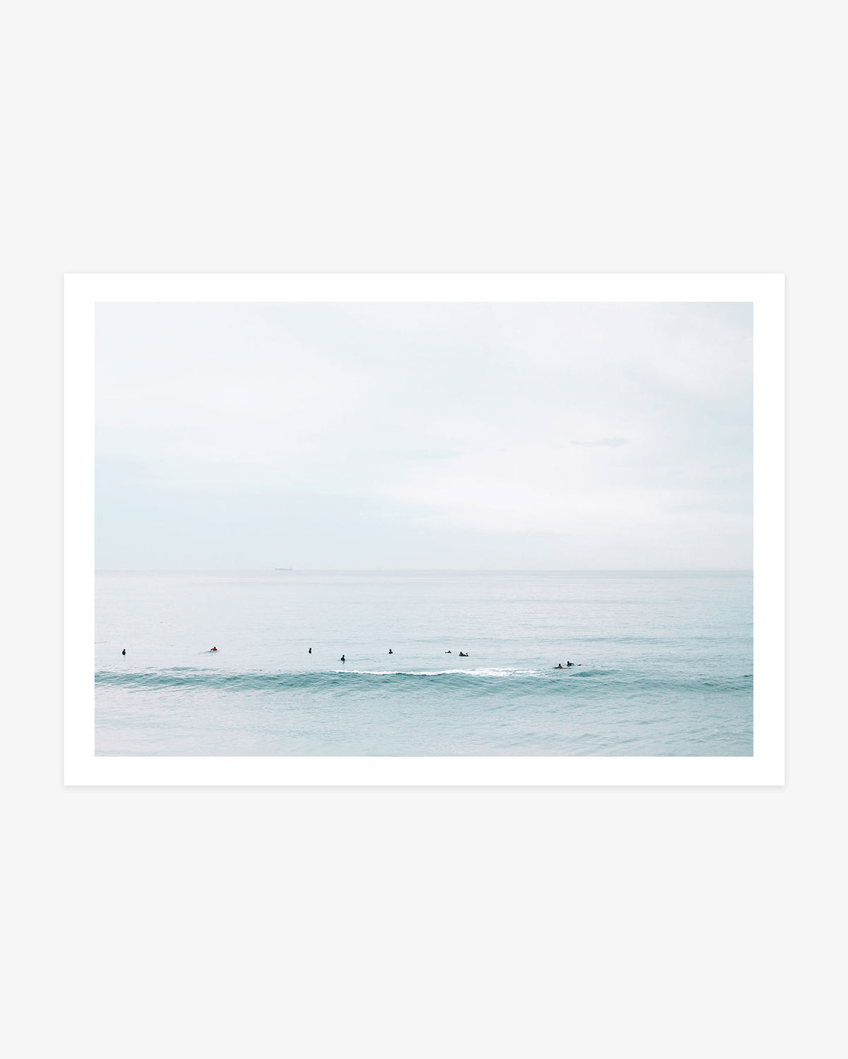 Huntington Beach surfers wall art featuring a small lineup waiting beyond a soft turquoise wave beneath a pale blue coastal sky.