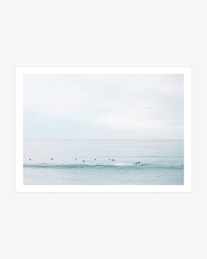 Huntington Beach surfers wall art featuring a small lineup waiting beyond a soft turquoise wave beneath a pale blue coastal sky.
