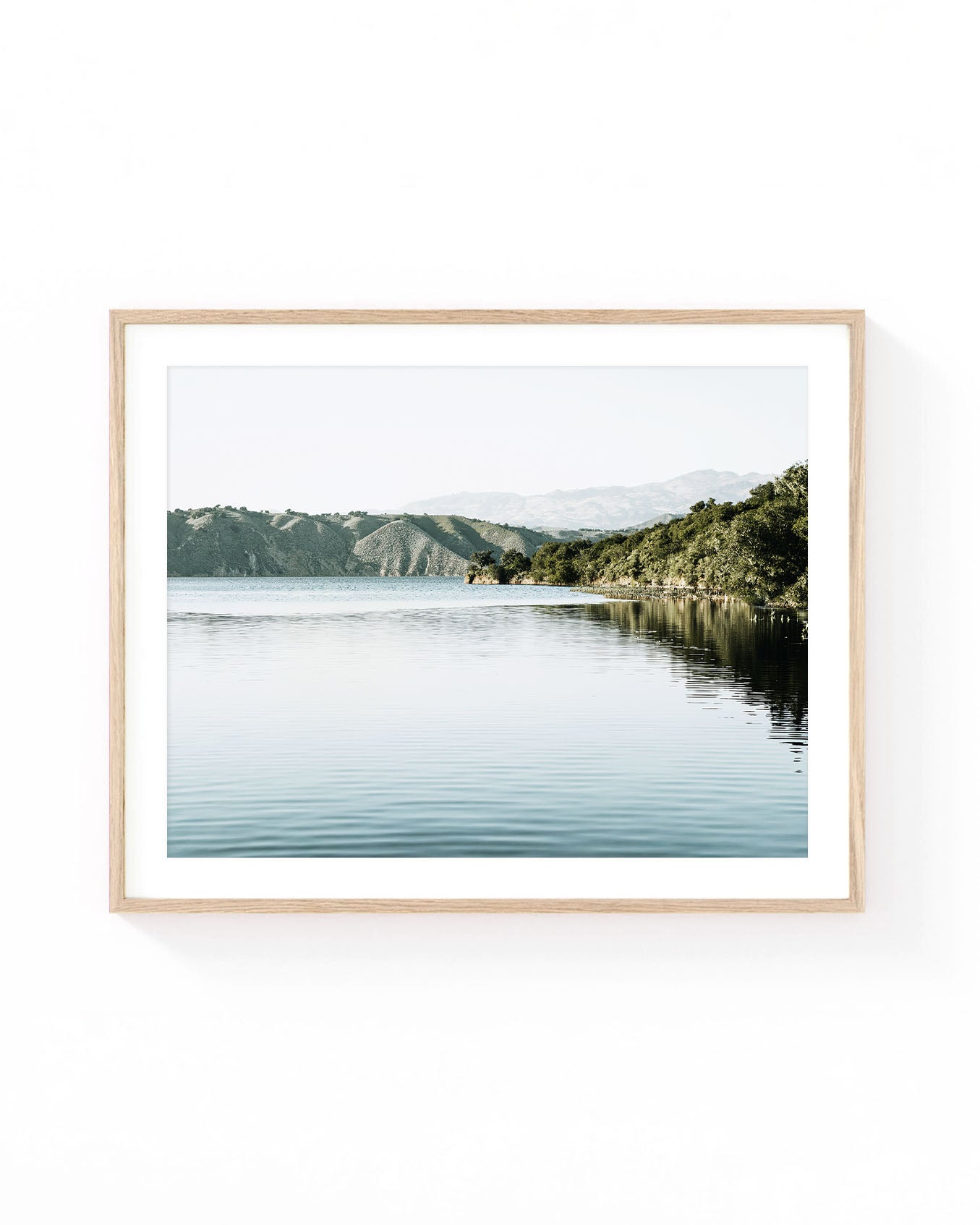Lake Cachuma with calm water reflections, rolling hills, and tree-lined shoreline under a soft neutral sky in California.