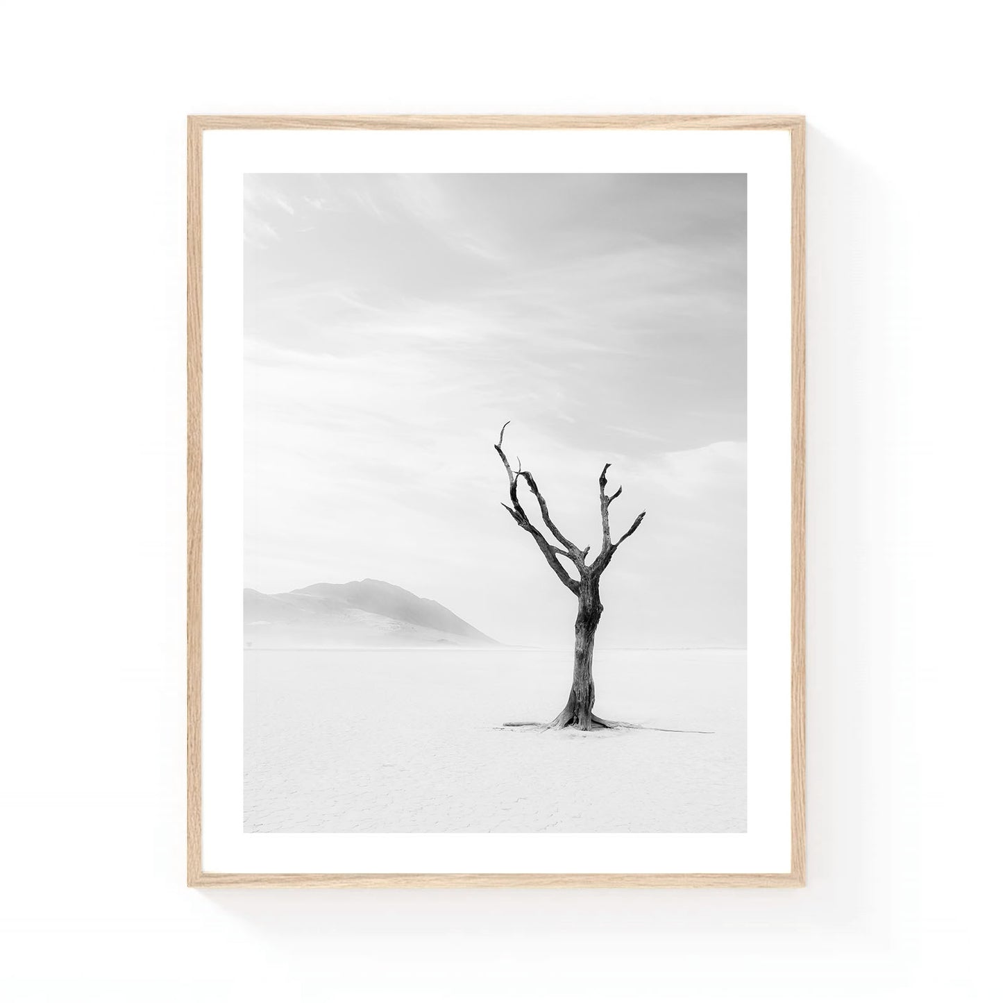 Minimalist black and white desert wall art featuring a solitary tree standing on a vast dry lake bed with distant mountains fading into soft atmospheric haze.
