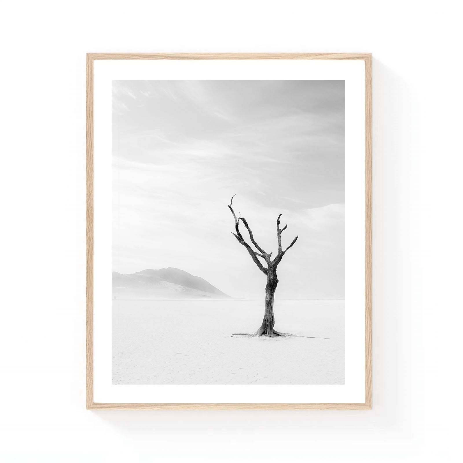 Minimalist black and white desert wall art featuring a solitary tree standing on a vast dry lake bed with distant mountains fading into soft atmospheric haze.