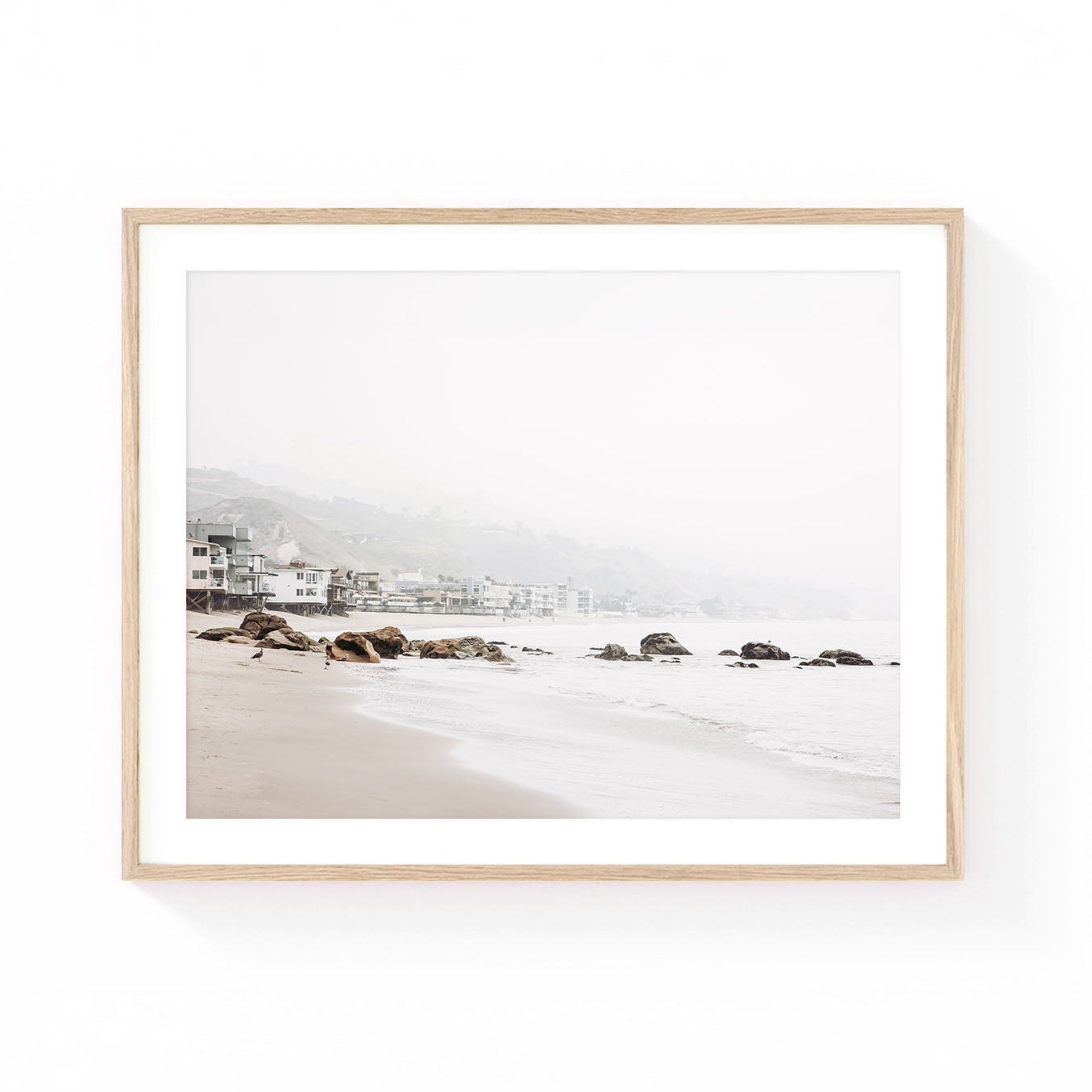 Malibu beach wall art featuring a quiet sandy shoreline, coastal homes, rocky outcroppings, and soft foggy ocean views in neutral coastal tones.