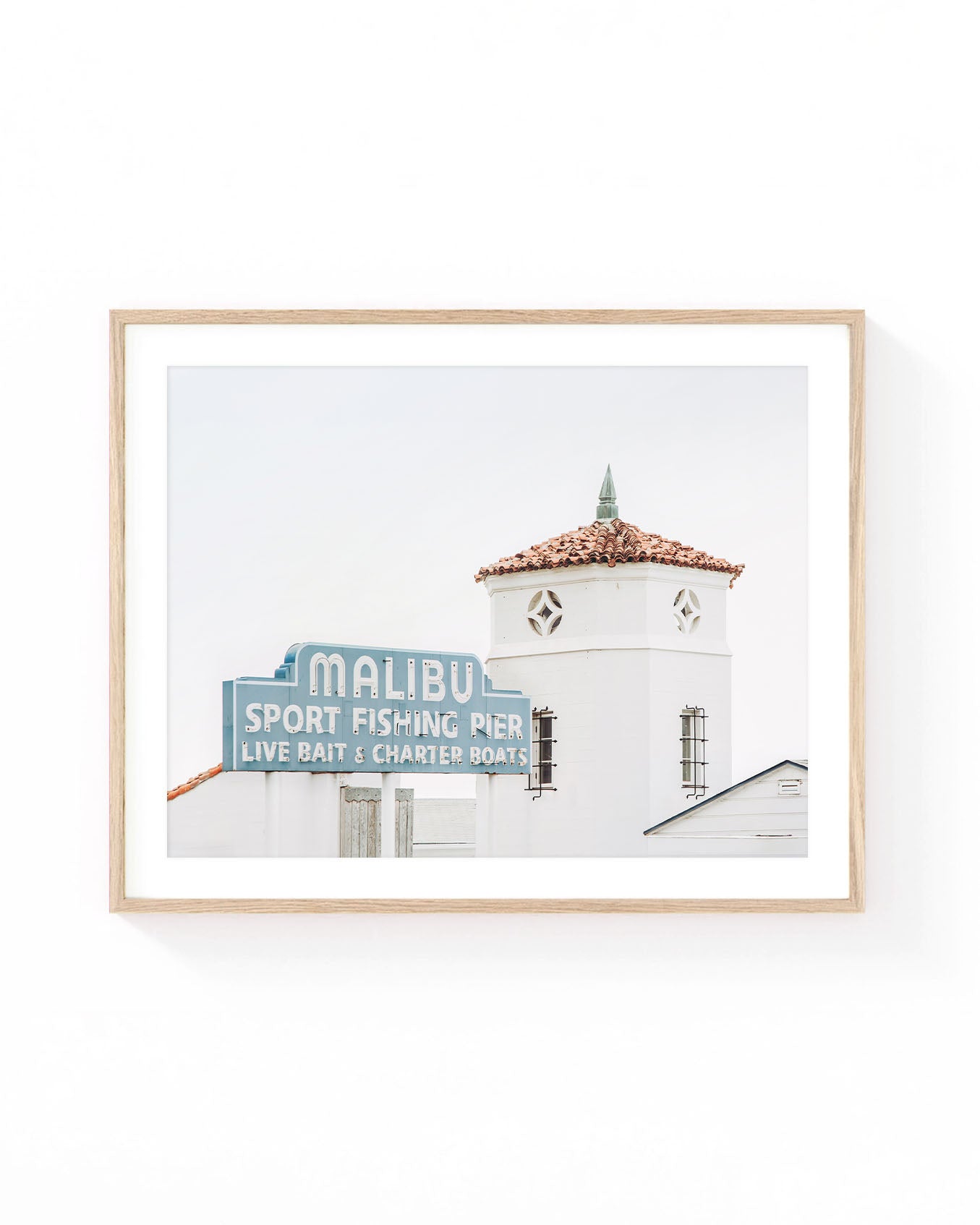 Malibu Pier wall art featuring the vintage Malibu Sport Fishing Pier sign beside a white coastal tower with a terracotta tile roof. Soft neutral California beach photography in muted blue, white, and warm terracotta tones.