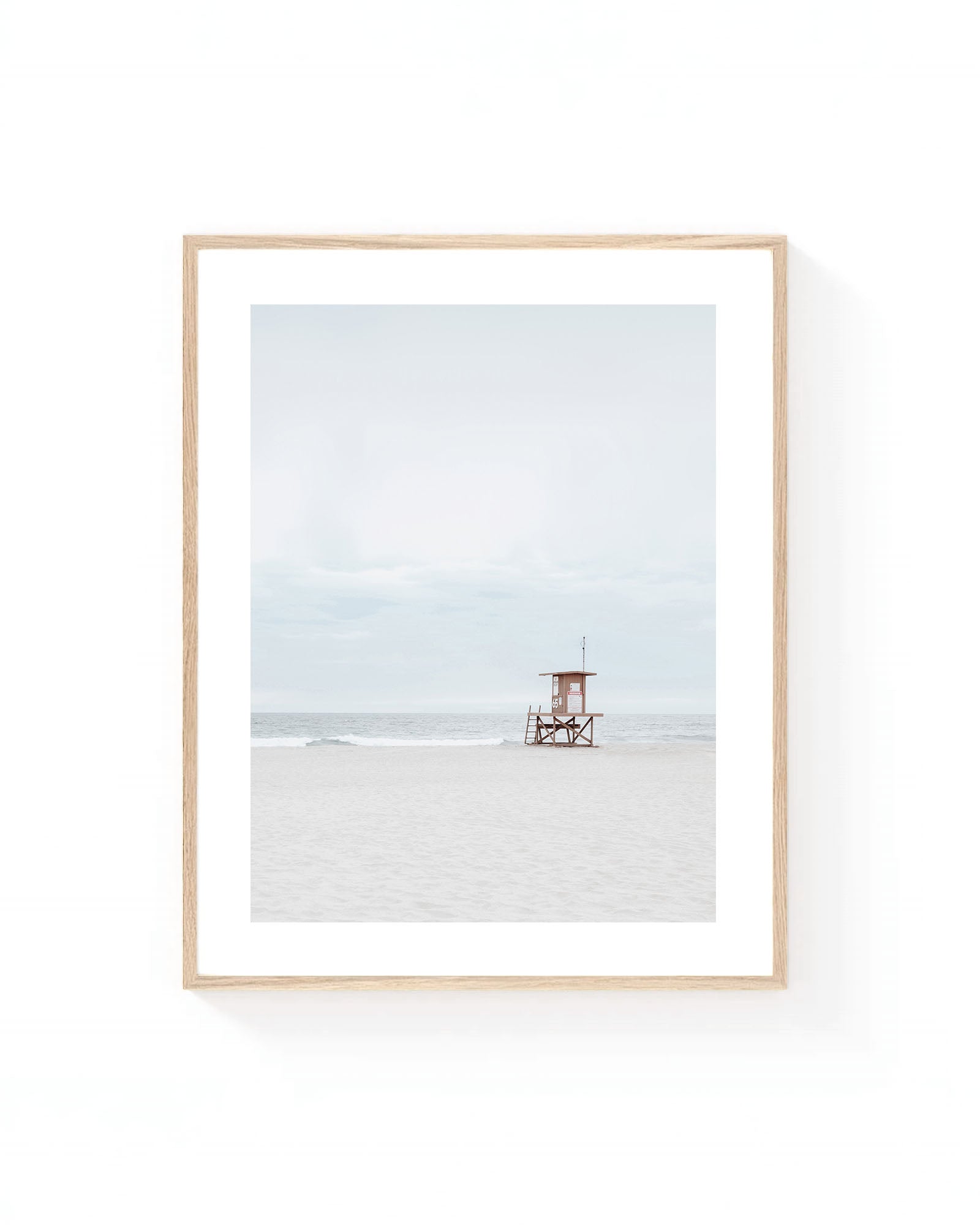 Minimalist lifeguard tower wall art on a quiet sandy beach with soft gray skies, gentle ocean waves, and neutral coastal tones.