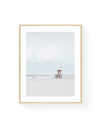 Minimalist lifeguard tower wall art on a quiet sandy beach with soft gray skies, gentle ocean waves, and neutral coastal tones.