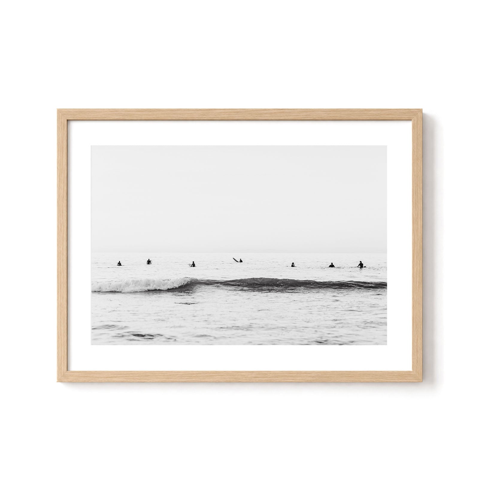 Minimalist black and white surf wall art featuring surfers waiting in the lineup beyond gentle breaking waves beneath an open ocean horizon.