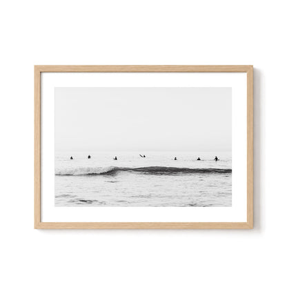 Minimalist black and white surf wall art featuring surfers waiting in the lineup beyond gentle breaking waves beneath an open ocean horizon.