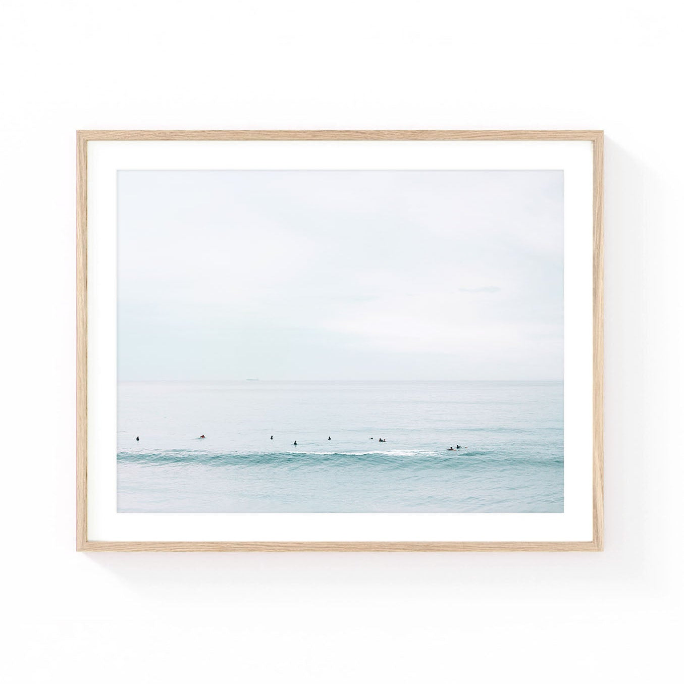 Minimalist surf wall art featuring surfers sitting in a calm ocean lineup beyond a soft rolling wave under a pale pastel sky.