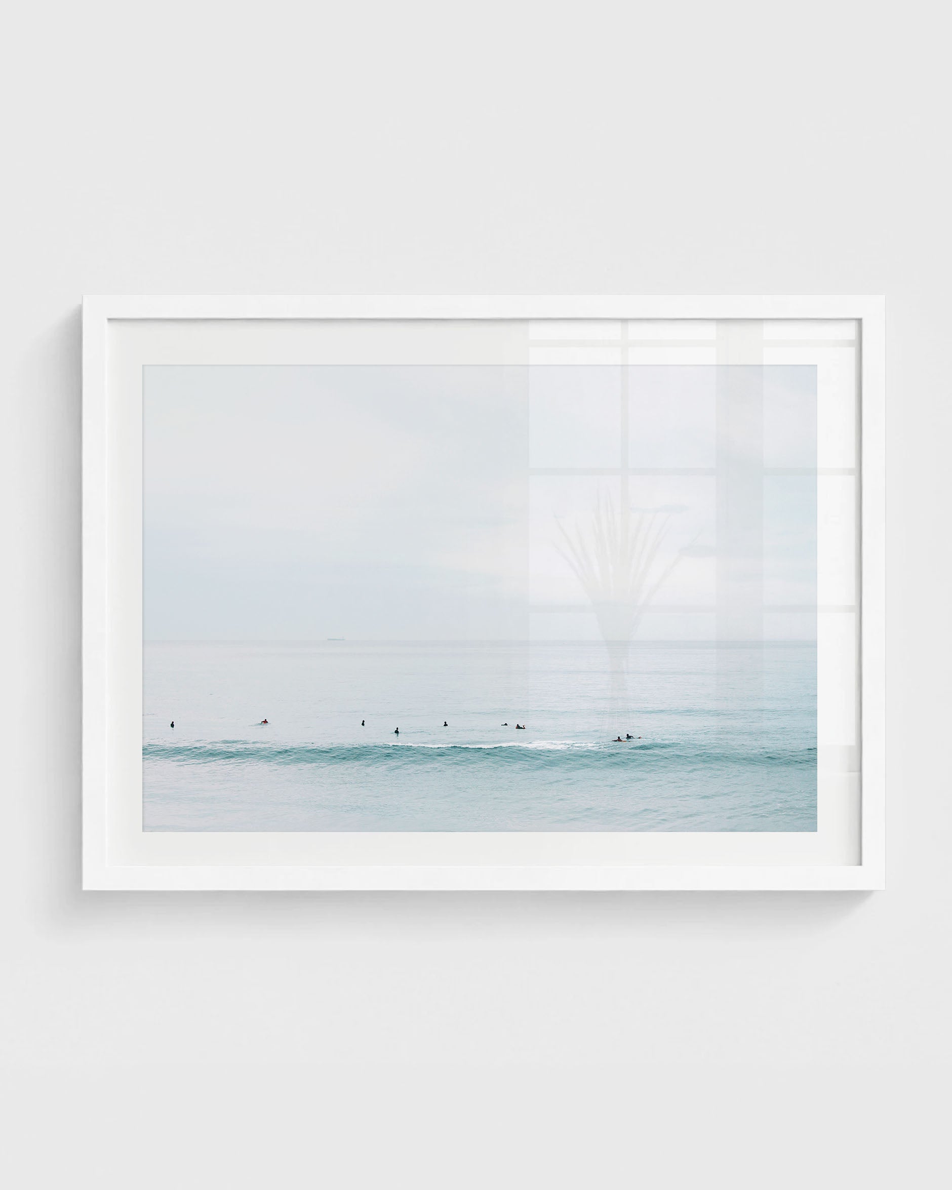 Minimalist ocean surf print featuring small silhouettes of surfers waiting in calm blue waves under a soft hazy sky.