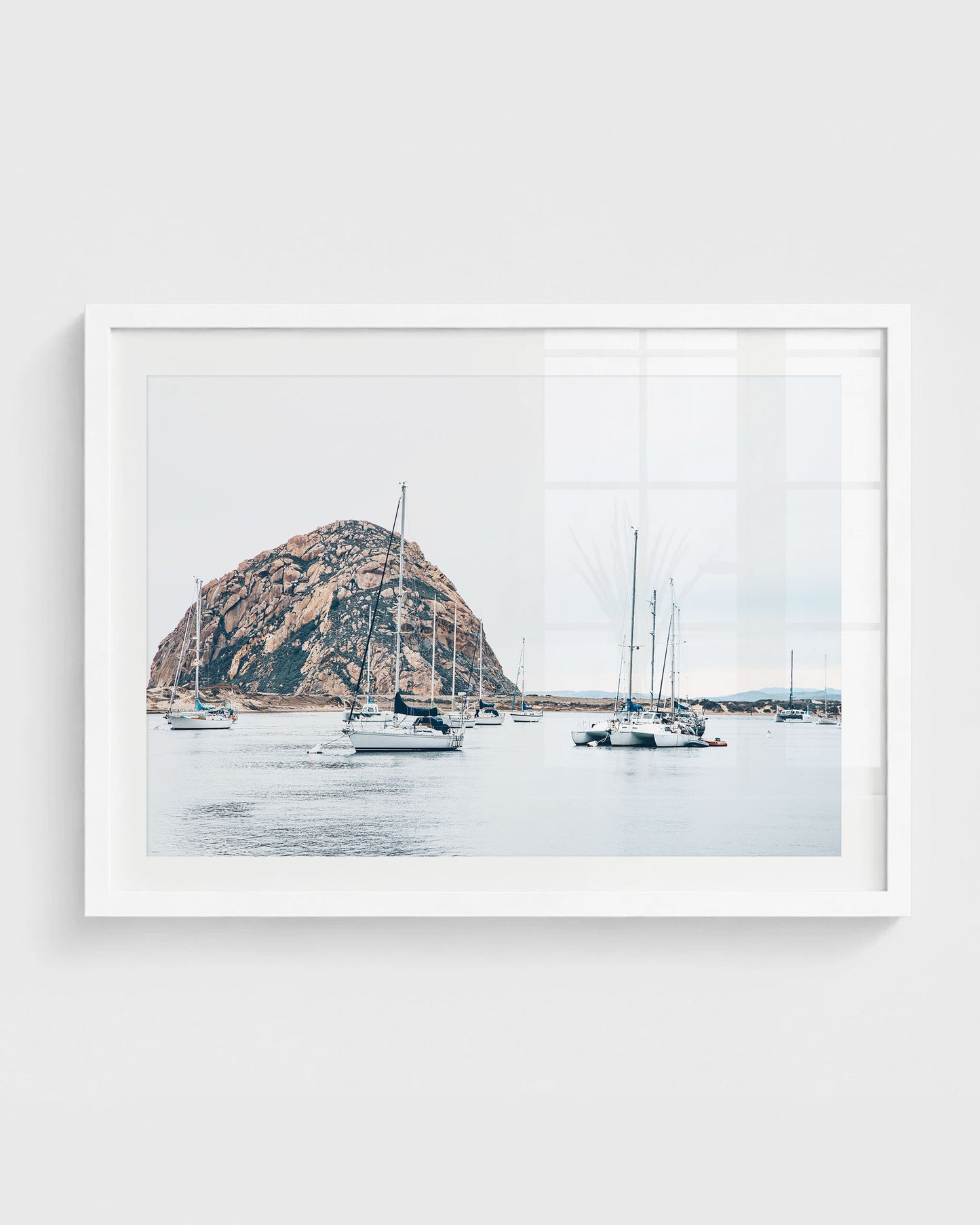 Morro Bay harbor with sailboats on calm water and Morro Rock rising in the background under a soft neutral sky.