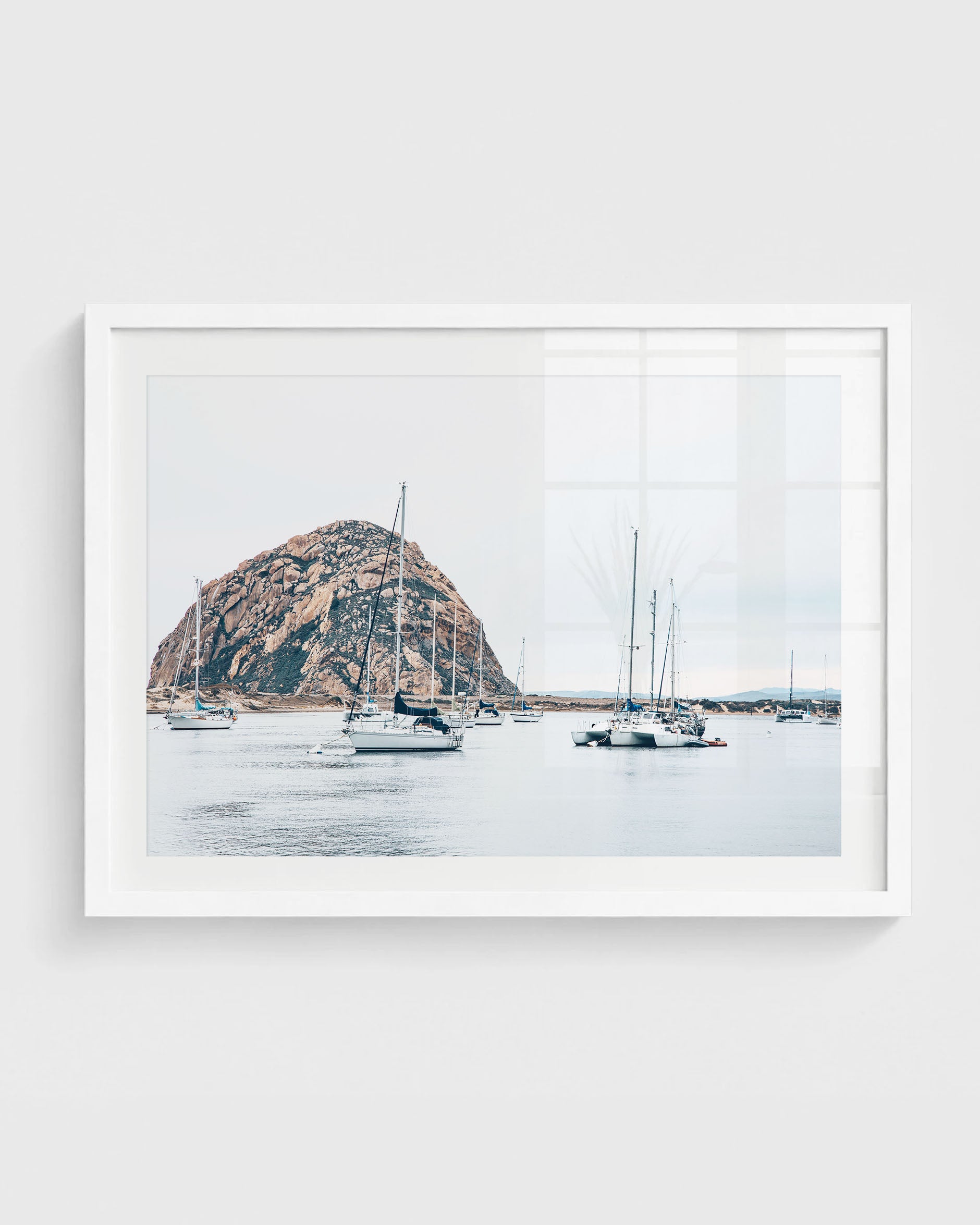 Morro Bay harbor with sailboats on calm water and Morro Rock rising in the background under a soft neutral sky.