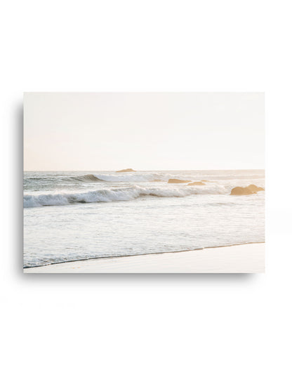 Neutral coastal wall art featuring gentle ocean waves rolling onto a sandy beach at golden hour, creating a serene seascape with soft natural light and calming coastal tones.