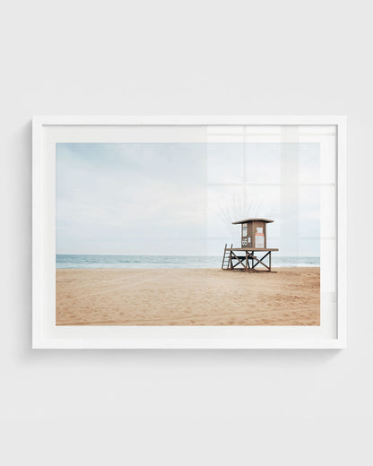 Newport Beach lifeguard tower on empty sandy beach with soft blue ocean and light cloudy sky.