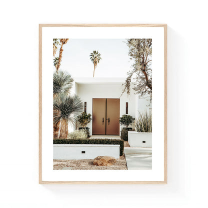Palm Springs front door wall art featuring a modern desert home entrance with bronze doors, sculptural desert plants, and tall palm trees in soft neutral tones.