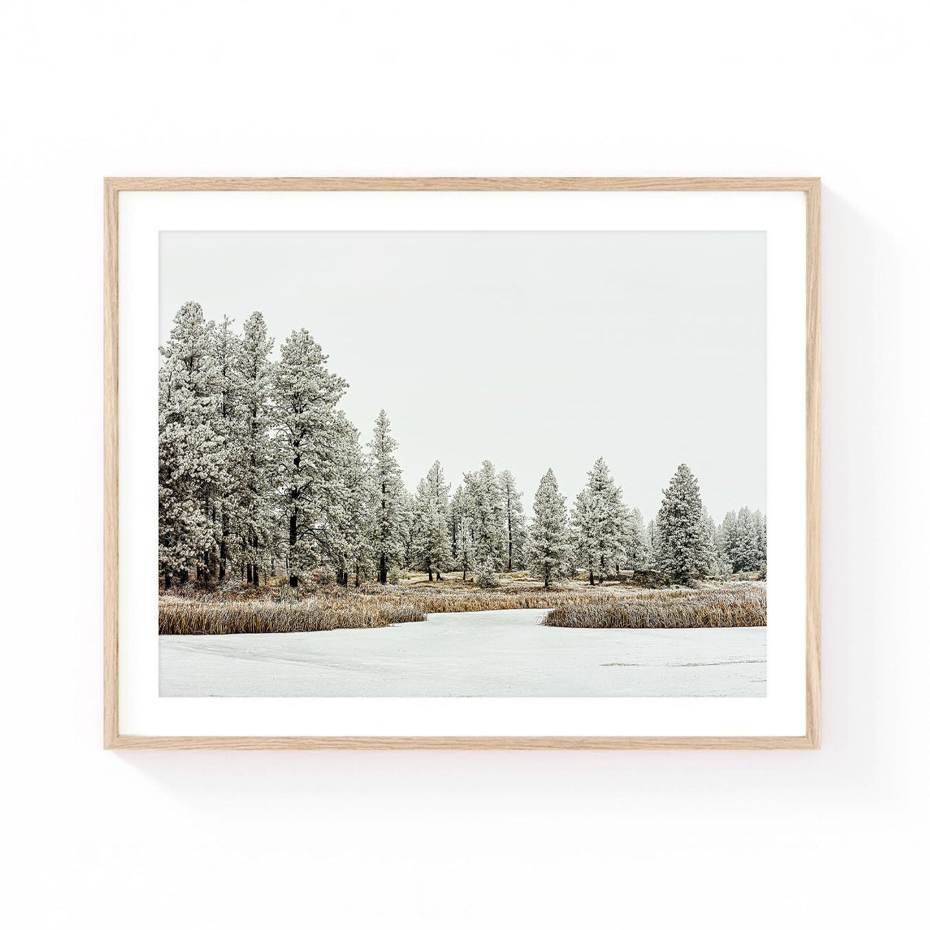 Winter forest wall art featuring snow-covered pine trees surrounding a calm meadow pond with soft neutral tones and a peaceful mountain atmosphere.