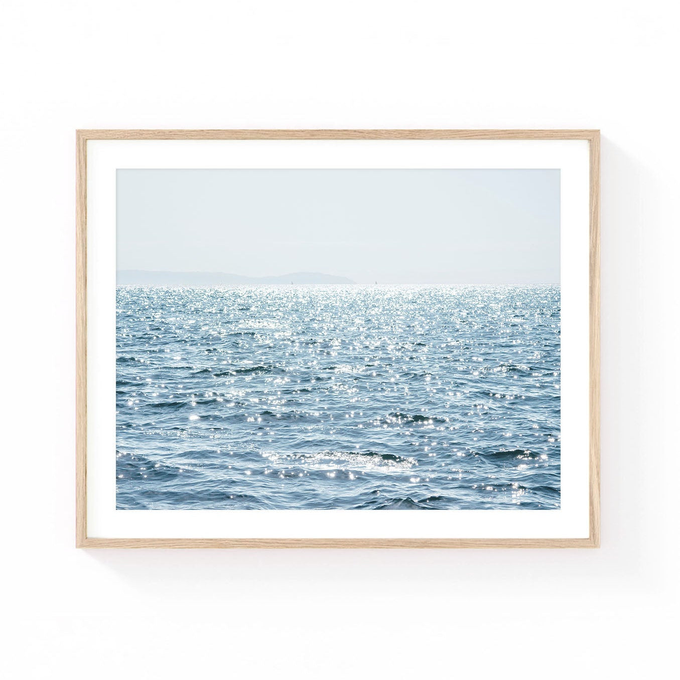 Ocean wall art featuring shimmering sunlight dancing across blue Pacific waters with a soft coastal horizon and airy sky.