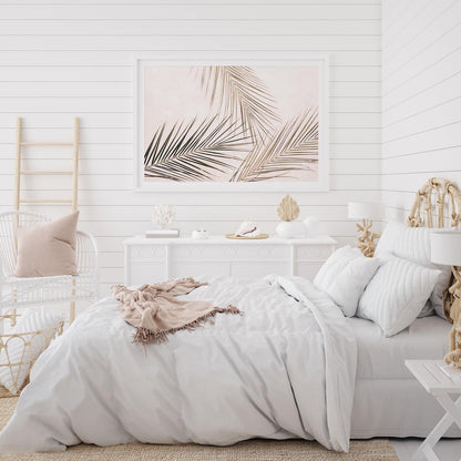Tropical palm leaves wall art print with blush background framed on a bedroom wall, styled as modern decor.